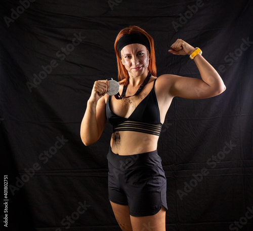 Beautiful redhead girl in sportswear with a silver medal in the studio on a black background