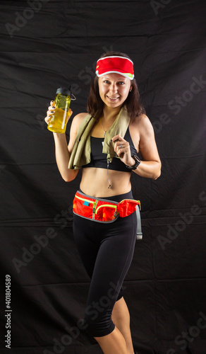 Beautiful girl in jogging red uniform, drinks water after training in the studio on a black background