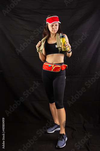 Beautiful girl in jogging red uniform, drinks water after training in the studio on a black background