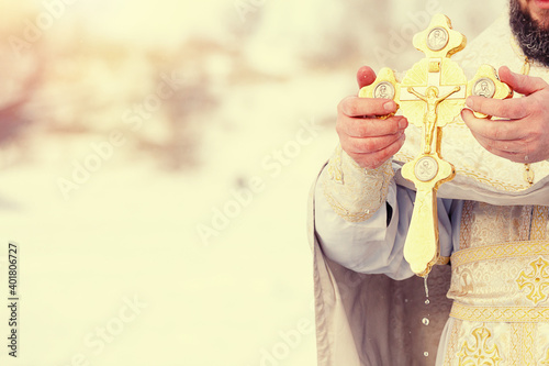 Billede på lærred The hands of a priest dip an Orthodox gold cross into the river