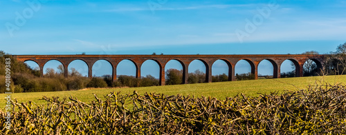 Peering over the hedgerow towards the Victorian railway viaduct for the London and North Western Railway at John O'Gaunt valley, Leicestershire, UK in winter photo