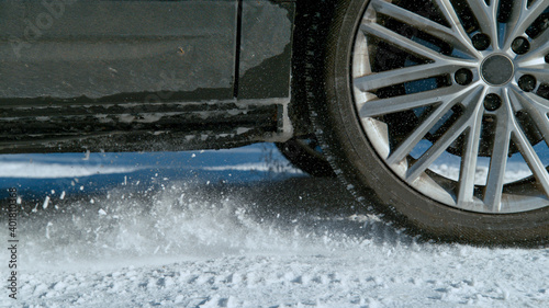 CLOSE UP: Wheels of blue car spin in place while trying to get traction on snow.