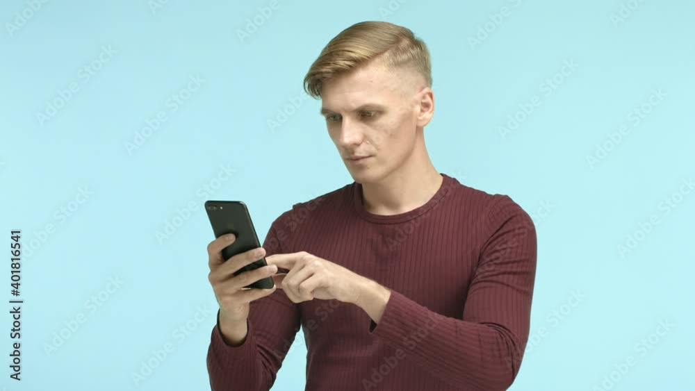 Handsome blond caucasian man casually browsing on smartphone then seeing something and staring at screen surprised, turn face at camera with happy smile, winning online prize Handsome blond caucasian man casually browsing on smartphone then seeing something and staring at screen surprised, turn face at camera with happy smile, winning online prize