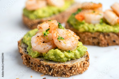 Obraz na plátně Healthy appetizer or snack avocado shrimp bruschetta with whole grain bread on white marble, closeup view