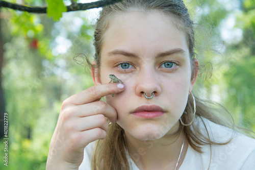 In summer, on a sunny day, a girl holds a gray lizard near her face ..