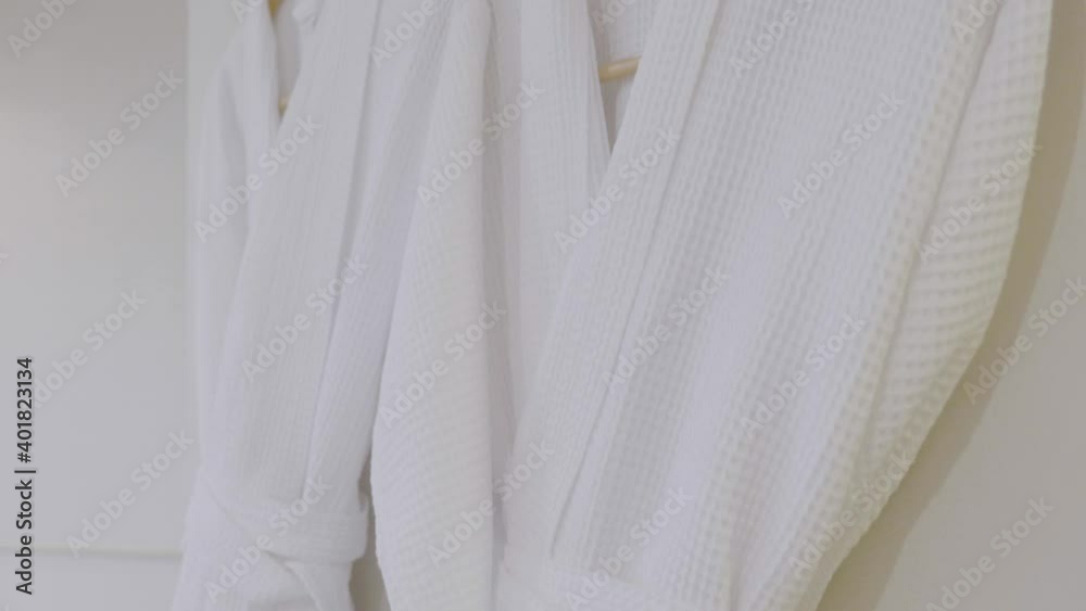 On a white bathroom wall, two comfortable robes are hanging for the next guests. On a white bathroom wall, two comfortable robes are hanging for the next guests.