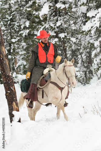 adult cowboy deer hunter riding white horse in mountain wilderness
