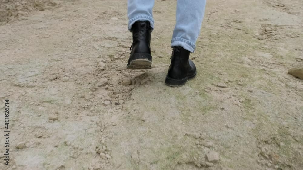 Male feet in black boots and jeans are walking on rocky ground Male feet in black boots and jeans are walking on rocky ground