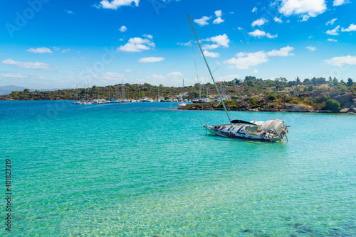 Overturned shipwrecked sunken sail boat yacht with seaweed growing on it in a sea bay. Vacation gone wrong. Greece