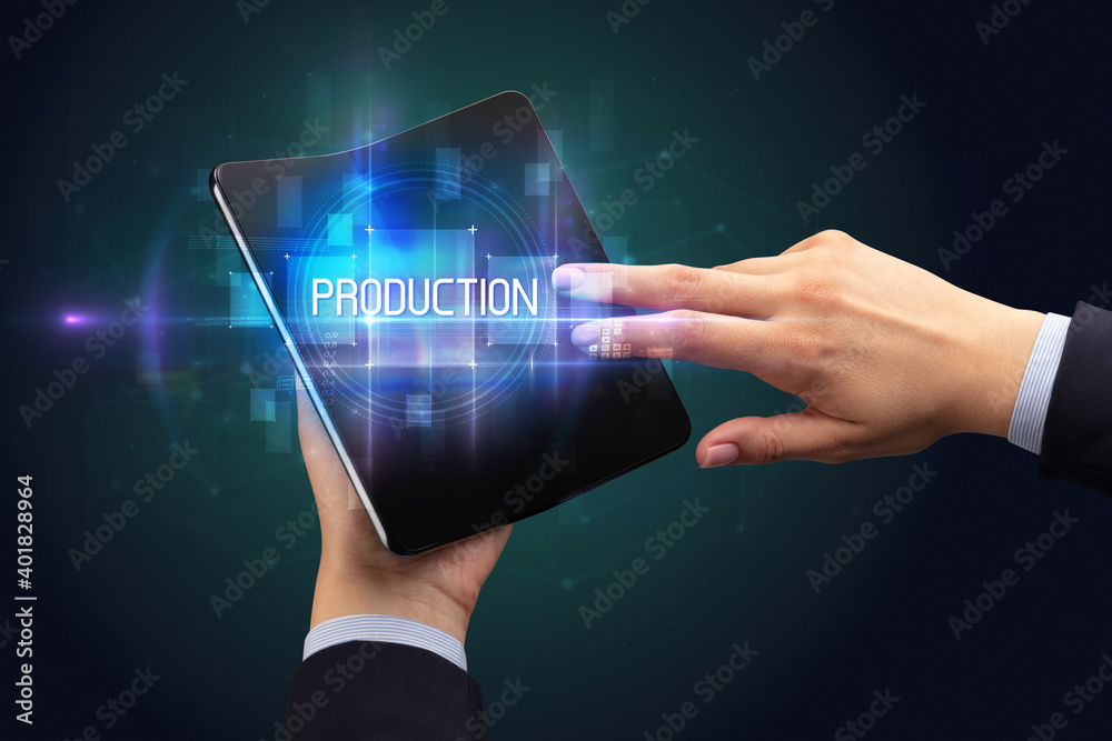 Obraz premium Businessman holding a foldable smartphone with PRODUCTION inscription, new technology concept