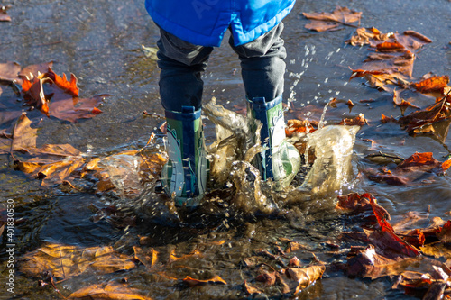 the legs of a child wearing wellies jumping in puddles splashing