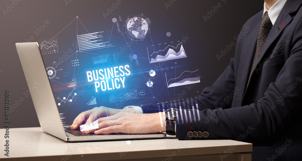 Businessman working on laptop with BUSINESS POLICY inscription, new business concept Businessman working on laptop with BUSINESS POLICY inscription, new business concept