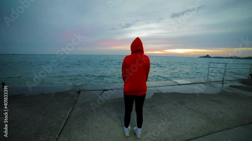 Girl in red hoodie relaxing by Lake Michigan and watching sunrise on clear blue sky and scenic seascape