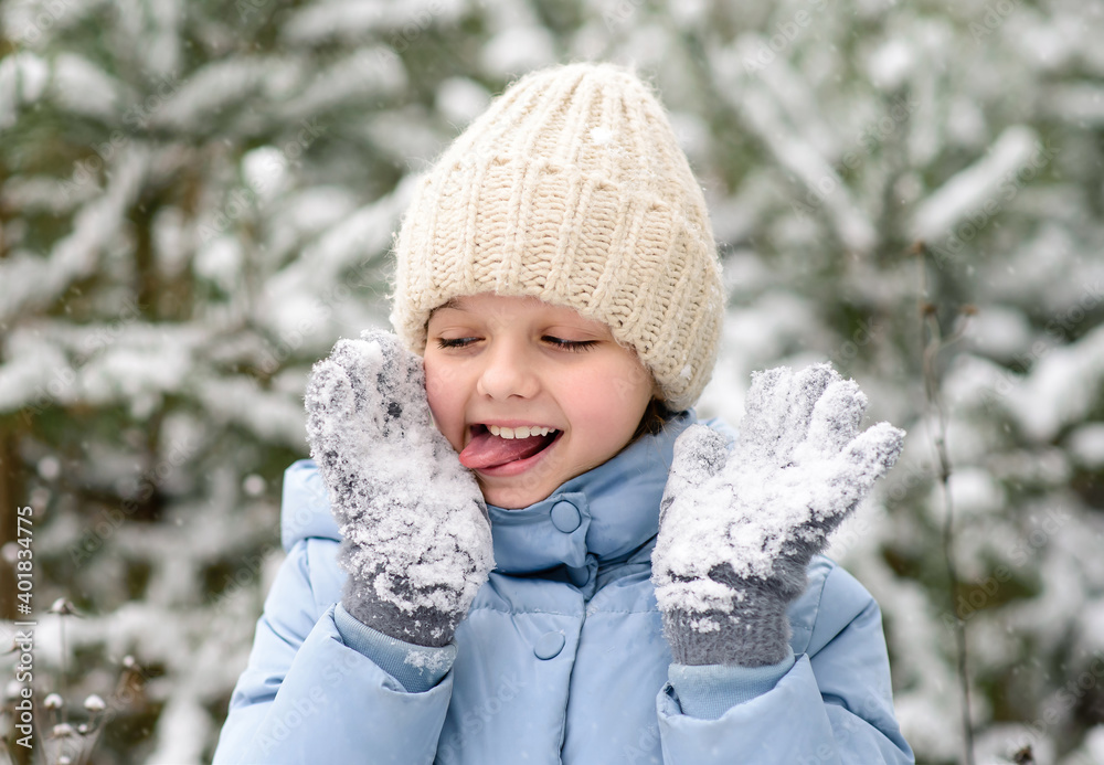 Happy little girl playing with snow on her mittens. A child in warm winter clothes. Walking and active rest in winter Happy little girl playing with snow on her mittens. A child in warm winter clothes. Walking and active rest in winter