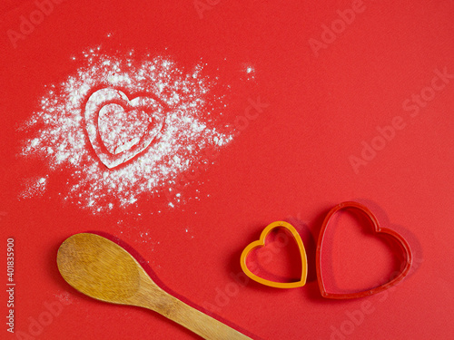 Bakery products. Flour is scattered on the table in the form of hearts. Form for gingerbread. Valentine's day baked goods flour scattered in the shape of a heart on a red background. Christmas 