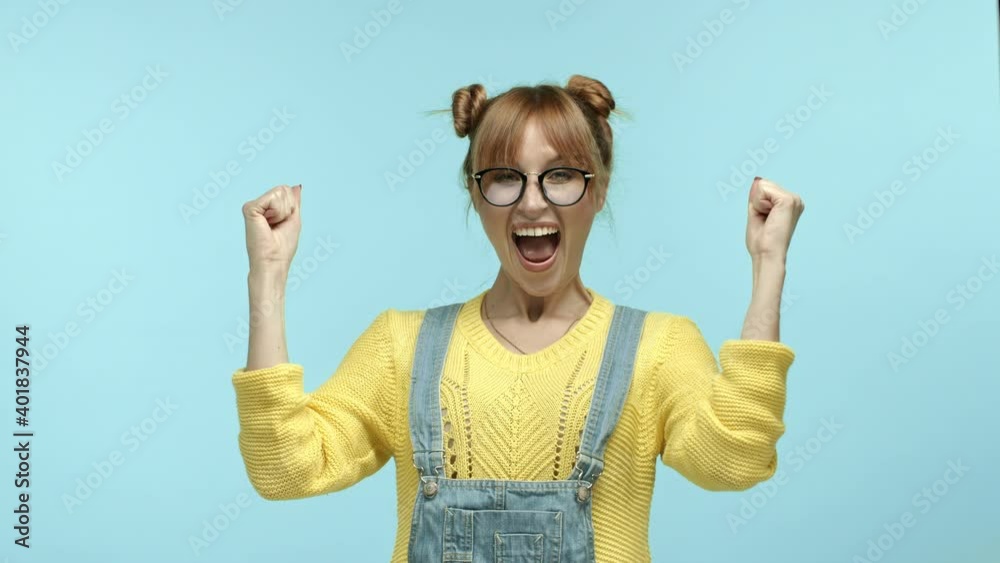Cheerful hipster girl winning and rejoicing, scream yes with joy and raising hands for fist pumps, achieve goal and success, enjoying triumph, standing over blue background