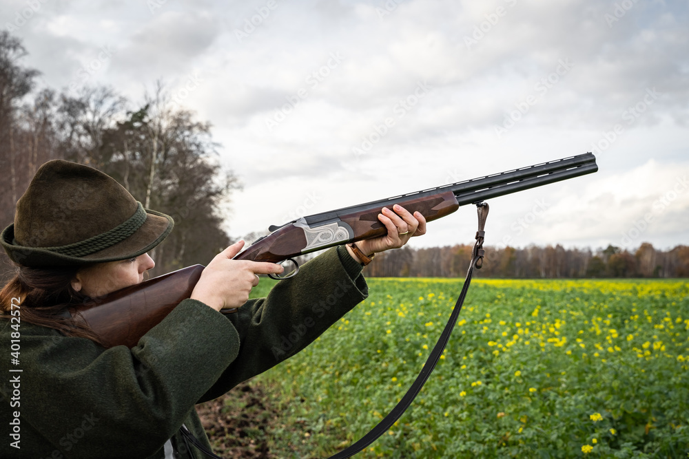Fototapeta premium Jagd und Wildhege - junge Jägerin zielt auf flüchtiges Wild, jagdliches Symbolfoto.