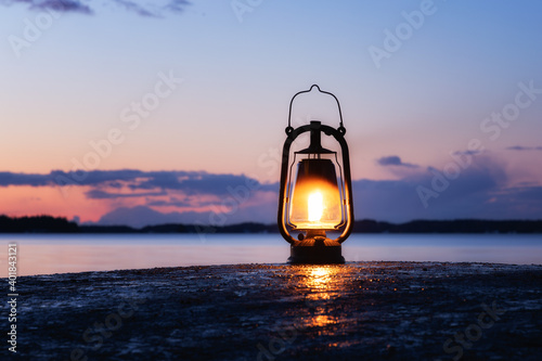 An old vintage oil lantern on a rock by the sea. Beautiful sunset sky and sea on background. Chill out travel concept. photo