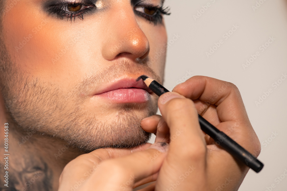 Hand of makeup artist with black kohl applying it on lips of male fashion model