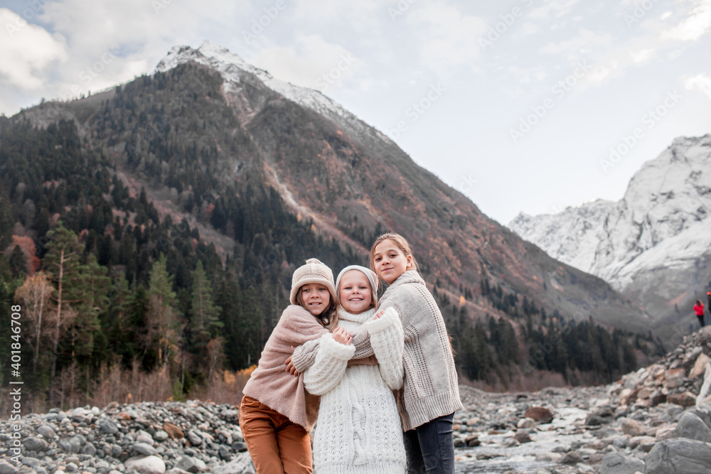 Group of kids hugging and walking outdoor in the nature against the river and beautiful mountains in snow, alpine view