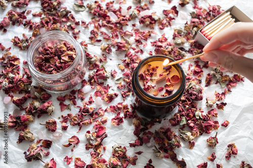 Handmade ecological and vegan soy wax candle on a white background with dried roses and rose quartz. Hand lighting with a match. Product cruelty free. photo