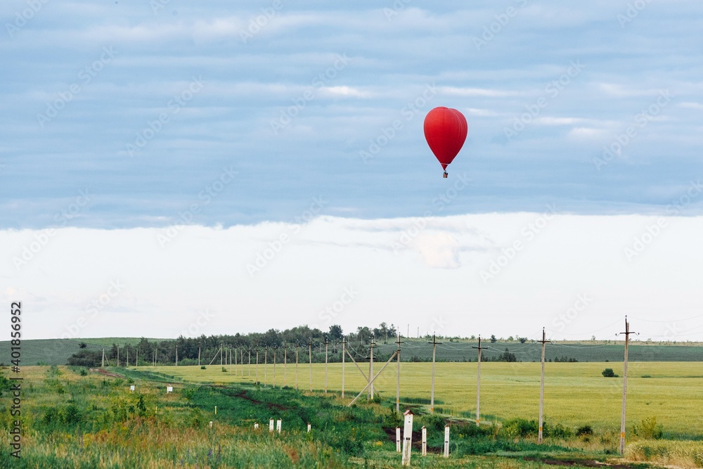 Fototapeta premium Red hot air balloon in shape of heart is landing on the green field