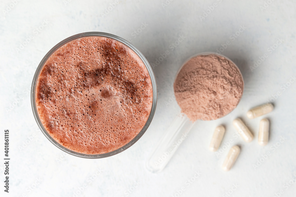 Glass with milkshake of whey protein isolate, protein powder in scoop, white capsules of amino acids and creatine, bodybuilding food supplements on white background, top view, flat lay Glass with milkshake of whey protein isolate, protein powder in scoop, white capsules of amino acids and creatine, bodybuilding food supplements on white background, top view, flat lay