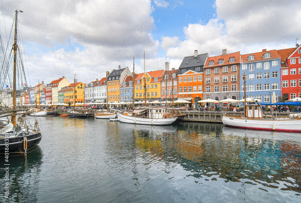 Tourists sightsee, shop and dine at sidewalk cafes on an autumn day on the 17th century waterfront canal Nyhavn in Copenhagen, Denmark.