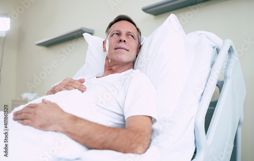 Thoughtful mature patient man is lying on the clinic bed in a hospital ward and looking away