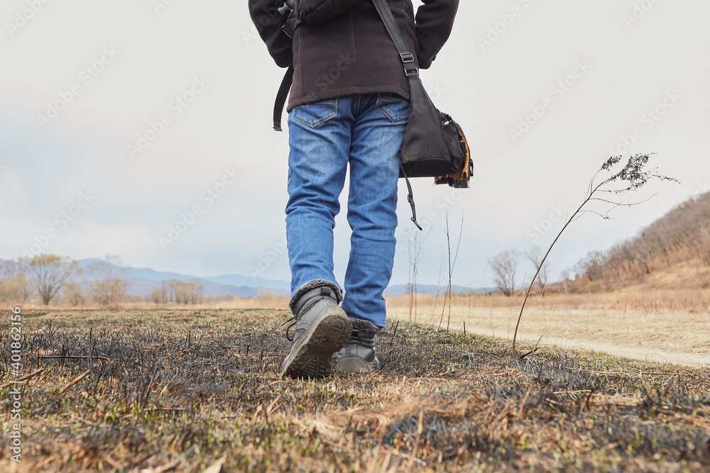 Walking on the scorched grass, a man in jeans and sneakers walks towards the road, bottom view Walking on the scorched grass, a man in jeans and sneakers walks towards the road, bottom view