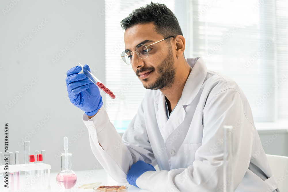 Gloved researcher looking at flask with several tiny samples of vegetable meat Gloved researcher looking at flask with several tiny samples of vegetable meat