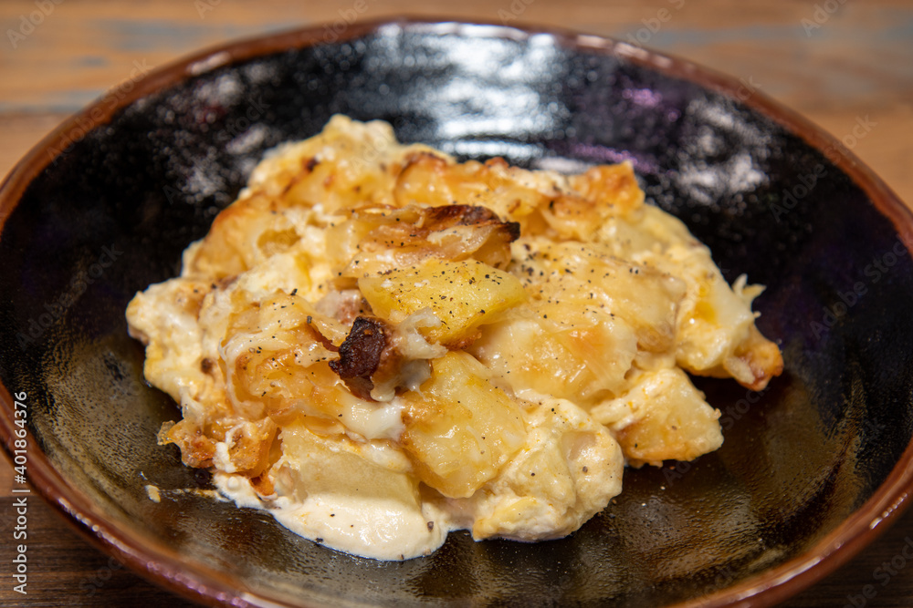 A delicious plate of Cheesy Chorizo Potato bake on a wooden restaurant work top A delicious plate of Cheesy Chorizo Potato bake on a wooden restaurant work top