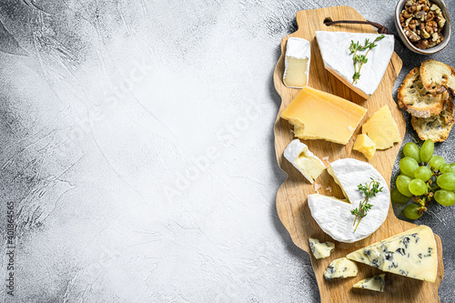 Assorted cheeses on a wooden cutting Board. Camembert, brie, Parmesan and blue cheese with grapes and walnuts. White background. Top view. Copy space photo