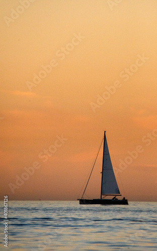 vertical image of orange sky at sunset and silhouette of sailboat in corona del mar beach orange county California