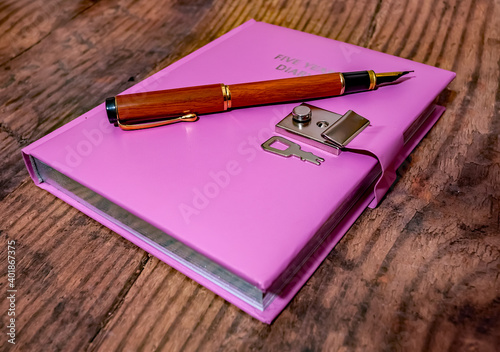A pink five year lockable diary and wooden fountain pen on a wooden background