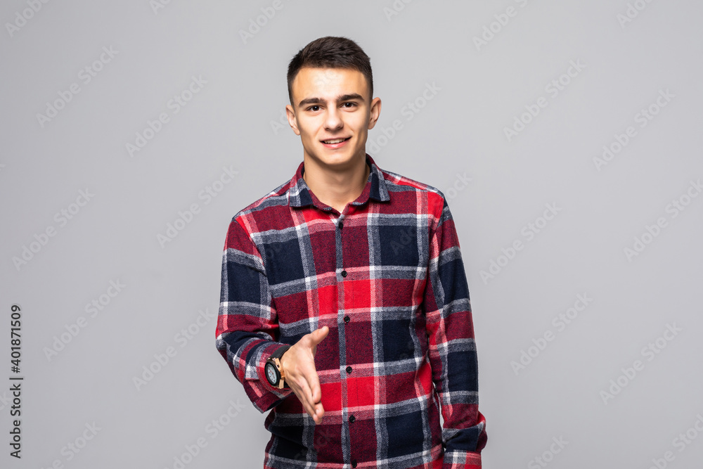 Smiling man in red shirt holds out his hand for a handshake and looking at the camera over gray background Smiling man in red shirt holds out his hand for a handshake and looking at the camera over gray background