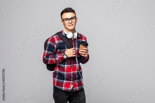 Young handsome man with backpack holding coffee cup isolated on gray background. Smiling student or businessman portrait.