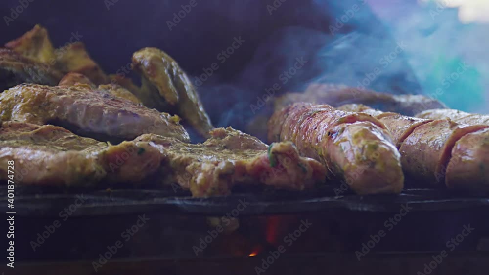 Unos deliciosos chorizos de chancho y pollo cubiertos de salsas y aceite vegetal  asándose en una parrilla cacera y grande en una casa de verano. Deliciosa comida. 