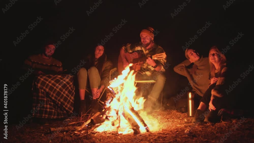 Picnic of young people with bonfire in forest in the evening. Cheerful friends singing songs and playing guitar. Picnic of young people with bonfire in forest in the evening. Cheerful friends singing songs and playing guitar.