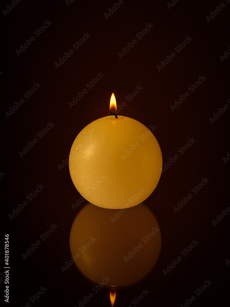 Single burning wax candle with flame and reflection on dark background Single burning wax candle with flame and reflection on dark background
