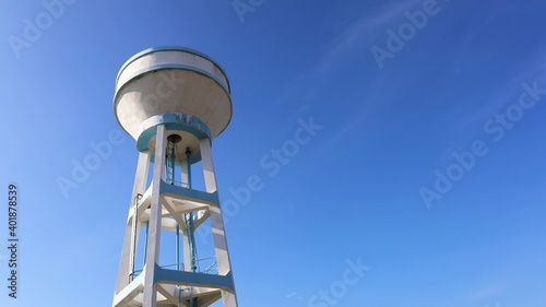 Concrete water tank on a tall tower. Large white storage tank for water supply systems in communities or workplaces. On a bright blue sky background with copy space. In view below. Selective focus