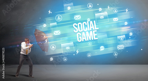 Handsome businessman defending with umbrella from SOCIAL GAME inscription, new age media concept