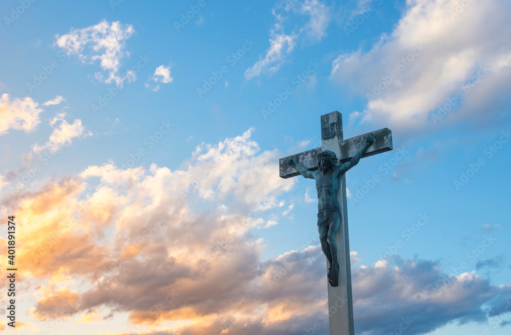 Jesus Christ on the cross against dramatic cloudy sky, at sunset. Crucifixion, religion and spirituality