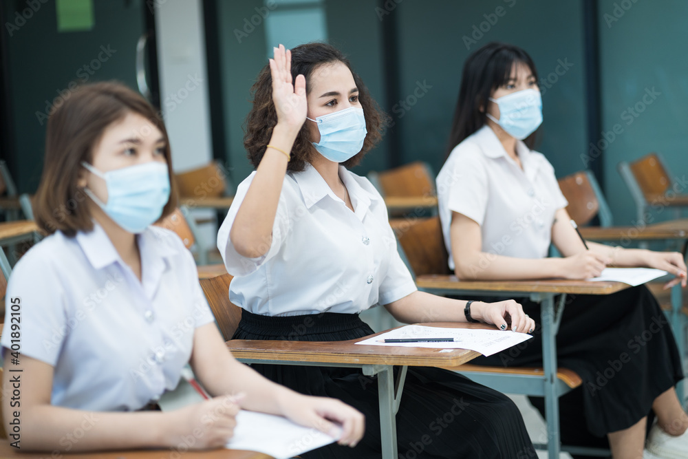 Fototapeta premium Cheerful college students in classroom wear protective face masks and use antiseptic for coronavirus prevention during coronavirus pandemic. Group of students wearing protection masks in class.