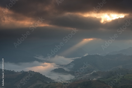 Gold light beam from cloud hole over a foggy mountain