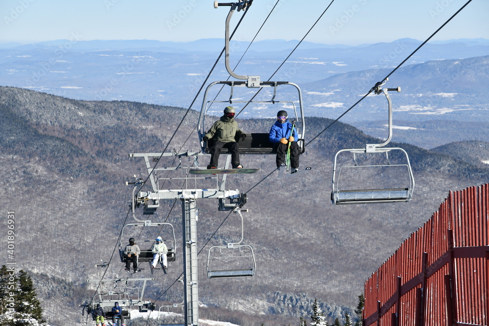Fototapeta premium Chairlift with people at Stowe Ski Resort in Vermont, view to the Mansfield mountain slopes, December fresh snow on trees early season in VT, hi-resolution image