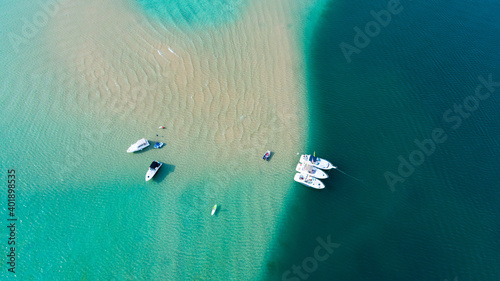 Aerial view of boats anchored on a sand bar in crystal clear blue water.