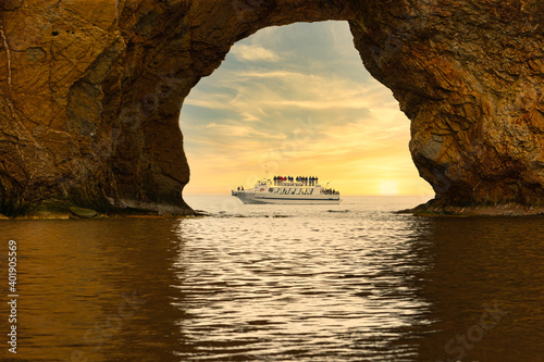 Boat transport tourism photographed by the cavity of the Percé Rock with a splendid sunset as a background.