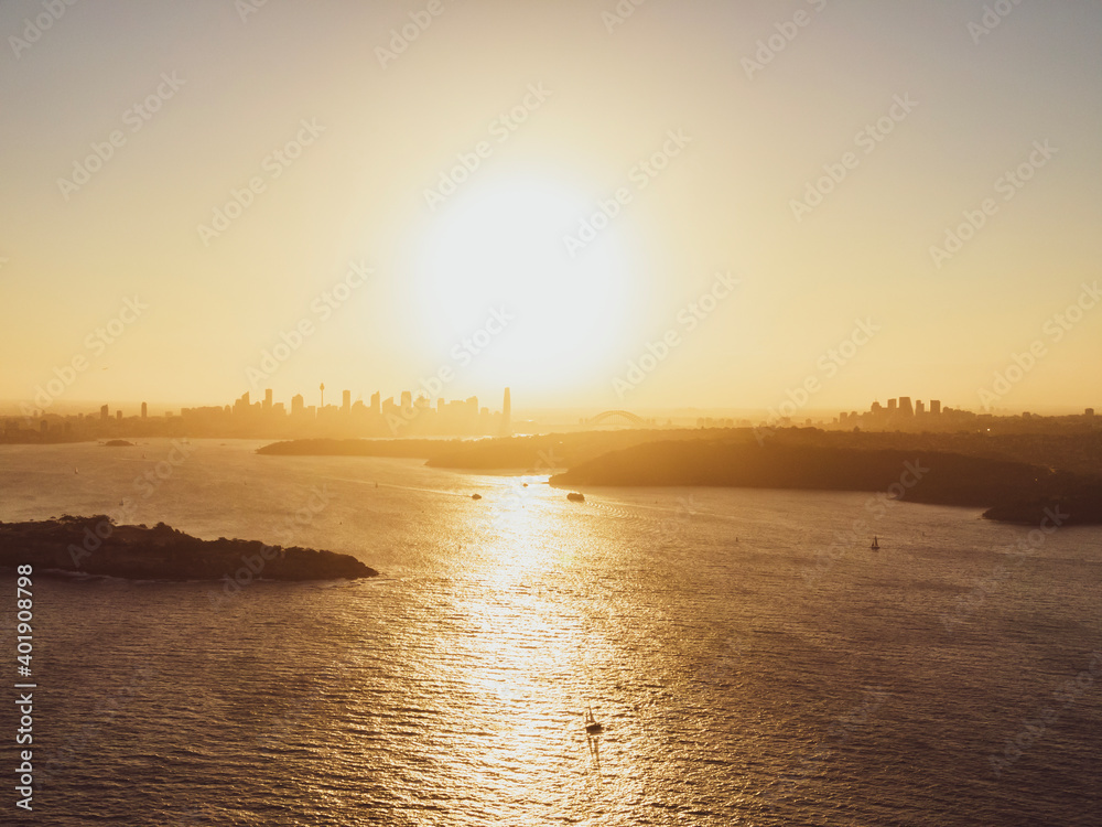 Fototapeta premium Panoramic sunset aerial drone view of famous Sydney Harbour with the CBD city centre skyline in the background. South Head, a headland to the north of Watsons Bay suburb, in the foreground.
