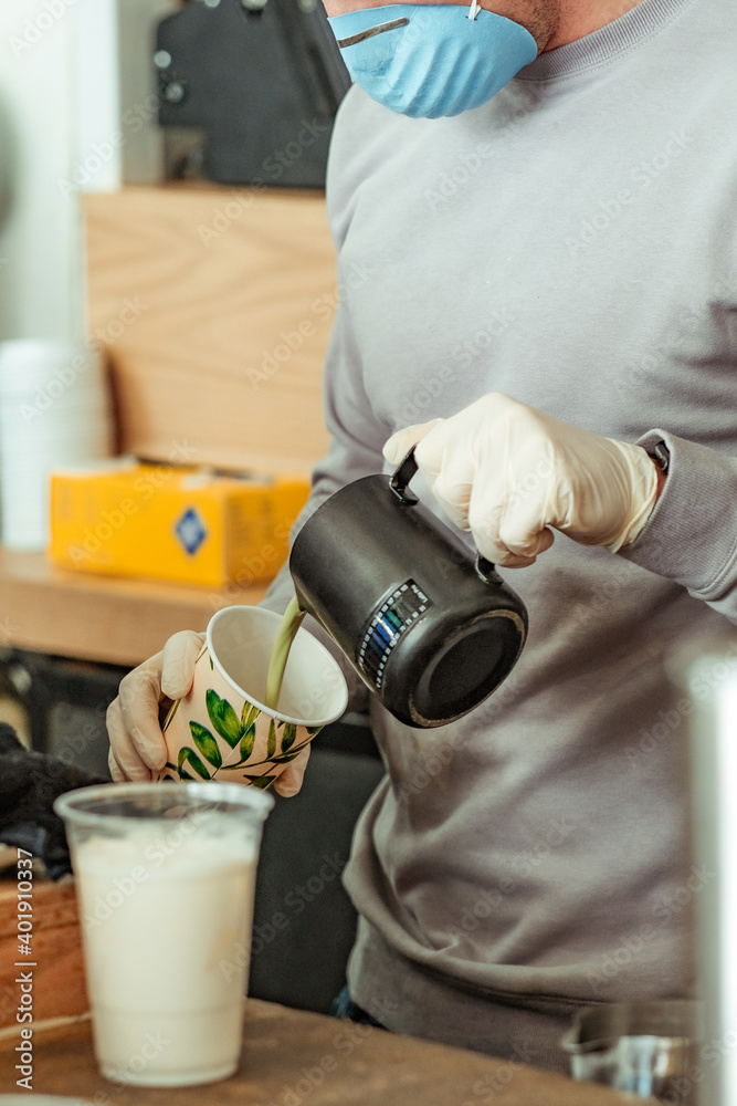 Fototapeta premium Barista at coffee shop restaurant wearing gloves and mask making drink to-go. New normal, small local business support concept